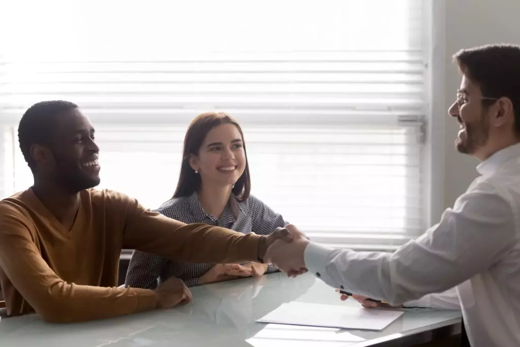 Young couple shaking hands with a lender over some paperwork